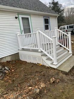 White deck with stairs leading to a side door of a white house.