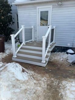 Exterior steps with white railing leading to a white door. Snow surrounds the deck.