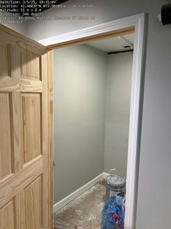 Open door reveals a small room with gray walls, white trim, and a concrete floor. A blue trash bag and bucket are visible.