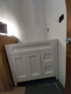 White bathroom vanity against a white wall in a room. Electrical box visible.