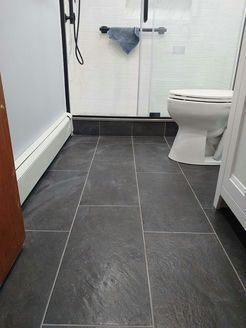Bathroom floor with gray rectangular tiles, white toilet, glass shower door, and white and gray walls.