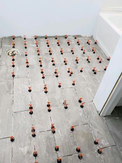 Tiles being installed in a bathroom, with leveling clips between tiles.