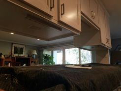 Kitchen cabinets over a counter covered with a dark blanket, view of a window and living room in the background.