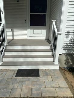 Exterior of a house with steps leading to the front door. Grey composite steps and a stone walkway.
