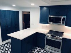 Navy blue kitchen with white countertops and a stainless steel oven. Black and white patterned floor.