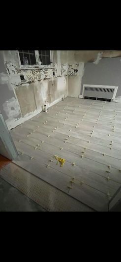 A room with bare wooden floors and damaged walls. A radiator sits in the corner.