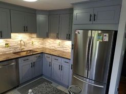 A modern kitchen with grey cabinets, stainless steel refrigerator, and granite countertops.