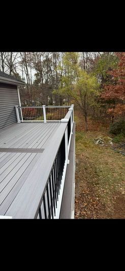 A gray deck with black railing overlooks a grassy area and trees with fall foliage.