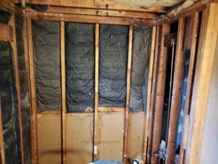 Interior of a bathroom under renovation: exposed wooden framing, black insulation, and lower panels of drywall.