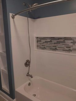 White bathtub and shower surround with blue accent wall, silver shower fixtures, and mosaic tile niche.