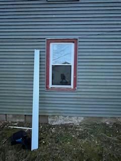 Exterior wall with a window and a piece of white trim lying on the ground.