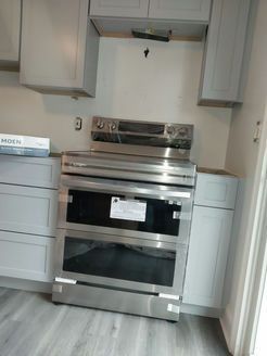 Stainless steel range oven installed between gray kitchen cabinets.