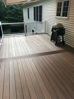 Wooden deck with grill, railing, and house. Natural wood tones.