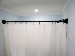 Black shower rod with white curtain, mounted on blue walls, white molding, and a ceiling light.