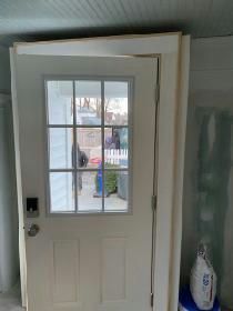 White door with glass pane, framed by unfinished trim. A person is visible through the glass.