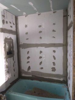 Bathroom renovation in progress, walls with drywall, gray grout, blue tub.