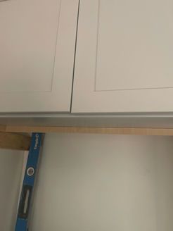 A level is used to check the alignment of a wooden board against white cabinet doors.