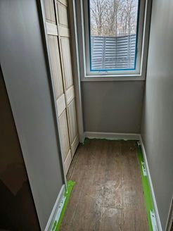 Narrow hallway with closet, window, and wood-look flooring. Walls are gray with green tape along the floor.