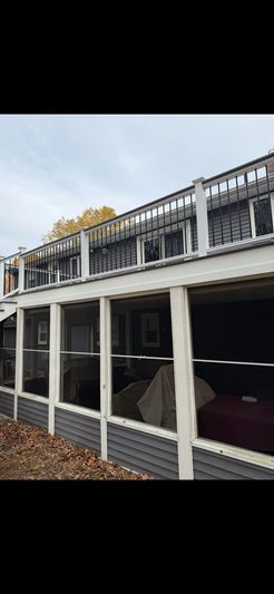 Exterior of a two-story building with a screened-in porch and a balcony with white railings, against a cloudy sky.