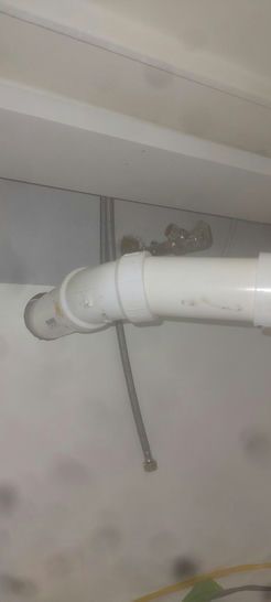 White plumbing pipes connected to a wall. A flexible pipe hangs down.