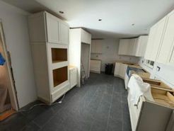Kitchen under construction with white cabinets, dark tile floor, and unfinished walls.