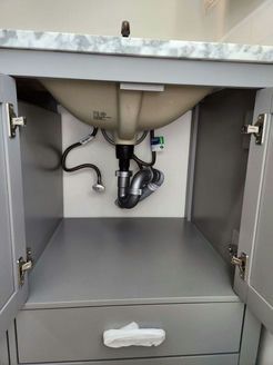 Gray bathroom vanity with open doors, revealing plumbing and sink basin.