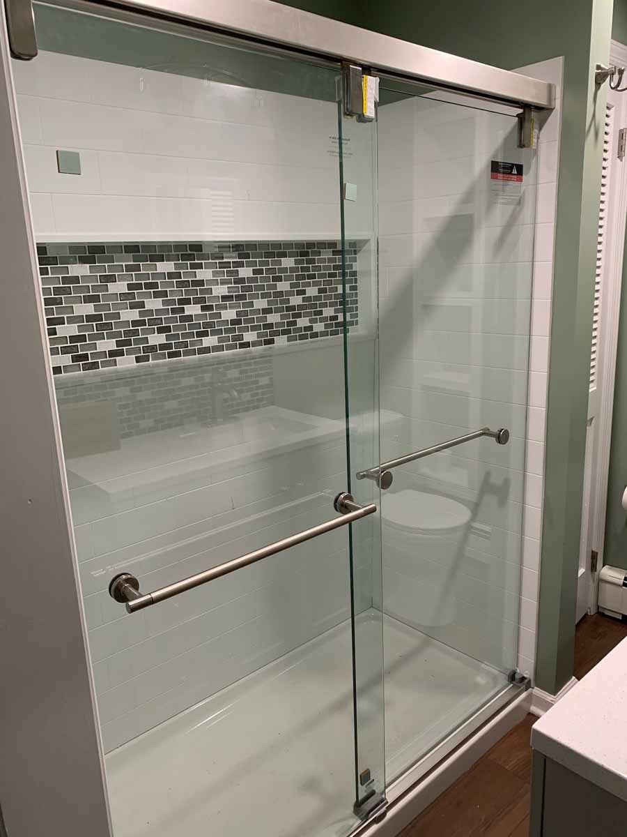 Shower with sliding glass doors, white walls, mosaic tile accent, and stainless steel grab bars.