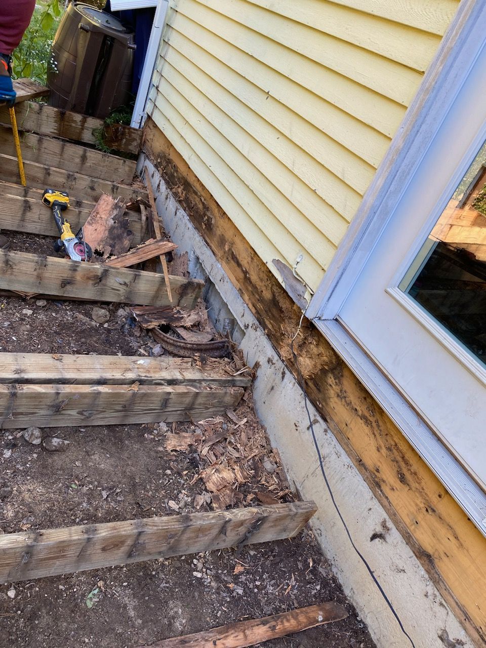 Outdoor wooden steps with rot damage, leading to a yellow-sided house with a door.