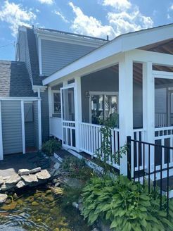 A house with a screened porch and a small pond in front. Light blue siding, white trim, and a black fence.