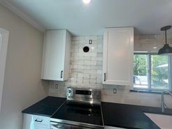 White kitchen cabinets flanking a stove on black countertops, tiled backsplash with a round vent.