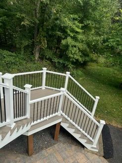 Composite deck with white railings and black balusters, steps, and surrounding greenery.