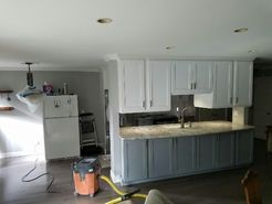 Kitchen with white upper cabinets, gray lower cabinets, and a vacuum cleaner in the foreground.