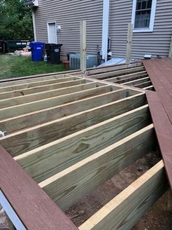Wooden deck under construction; green framing, brown decking, near house.