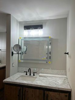 Bathroom vanity with a lighted mirror, sink, and dark fixtures against a gray wall.