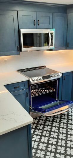 A kitchen with dark blue cabinets, white countertops, and black and white patterned floor; a stainless steel oven is open.