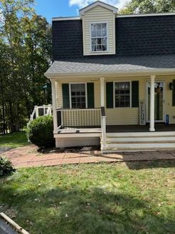 Yellow house with porch, black roof, and green shutters in a grassy yard.
