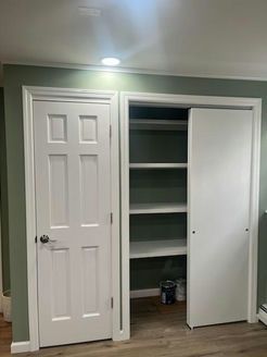 A room with a closed white door and an open closet with sliding door, white shelves, and green walls.