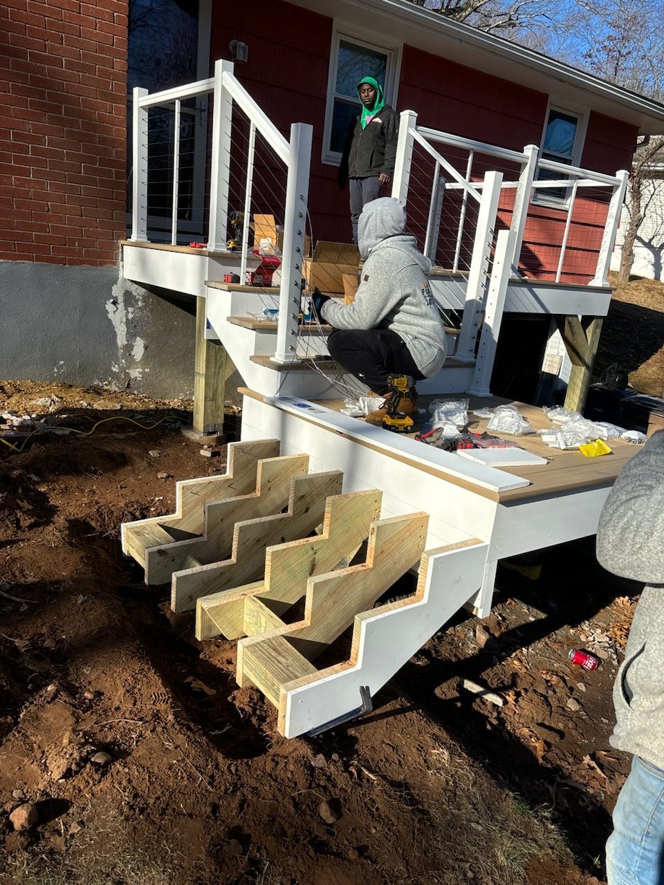 People building a wooden deck with stairs outside a red house.