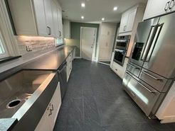 Modern kitchen with stainless steel appliances, dark gray floors, white cabinets, and a large sink.
