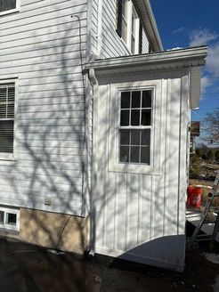 White house exterior with window and siding, a gutter, and shadows on the wall.