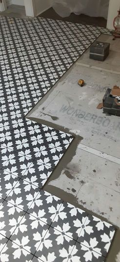 Floor tiling in progress with black and white flower pattern tiles on a concrete base.