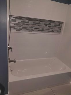 White bathtub with gray mosaic tile accent in a bathroom.
