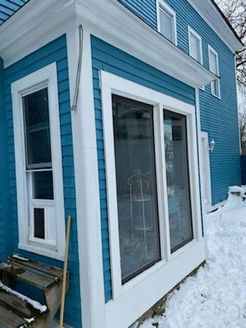 Blue house with white trim, sunroom with large windows, snow-covered ground.