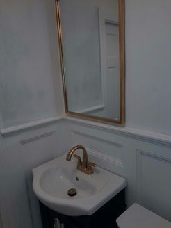 Small white bathroom with a gold-framed mirror over a white sink and gold faucet.
