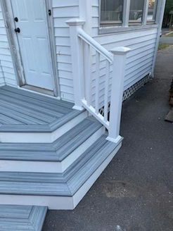 White house entrance with blue-gray deck stairs, white railing, and a door.