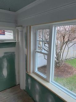 Interior room with white window frame, trim, and drywall, looking out to a backyard.