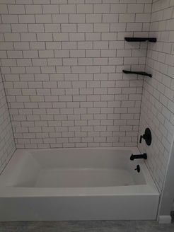 White tiled bathtub enclosure with black fixtures and shelves.