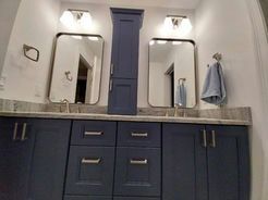 Bathroom with blue cabinets, mirrors, and a tall storage cabinet.