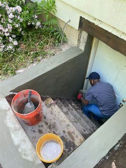 Person applying cement to basement stairs. Includes buckets and trowel. Exterior setting.