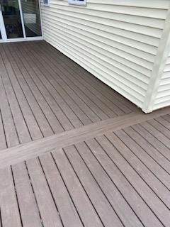 Wooden deck with light brown planks, next to a beige house with white siding and a glass door.